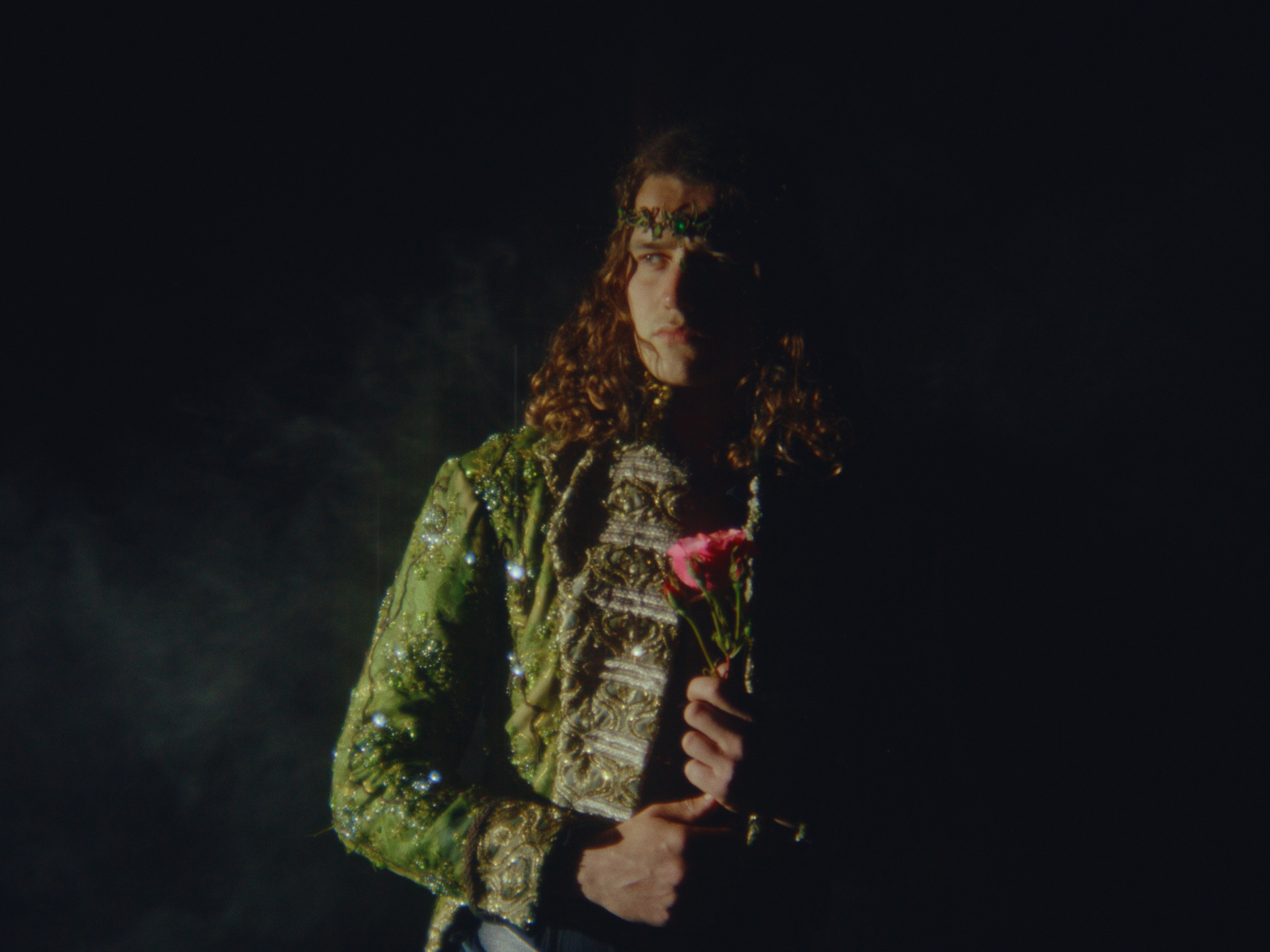 A figure in an ornate green costume holding a flower in near darkness — a TalesByTyler film still